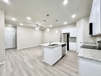 Kitchen with an island with sink, pendant lighting, ceiling fan, light wood-type flooring, and light stone countertops