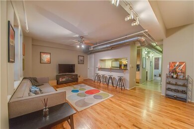 The large living room features a bar looking into the kitchen, exposed ductwork, and hardwood flooring. 