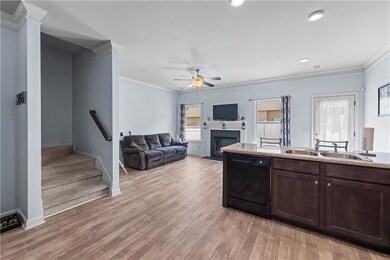Kitchen featuring black dishwasher, ornamental molding, a fireplace with flush hearth, a sink, and light wood-type flooring