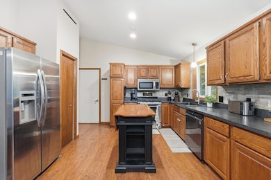 Spacious kitchen with vaulted ceilings, warm wood cabinetry, stainless stl appls, and a center island offering extra prep and storage space. Features modern tile backsplash, dark countertops, and plenty of workspace with natural light.