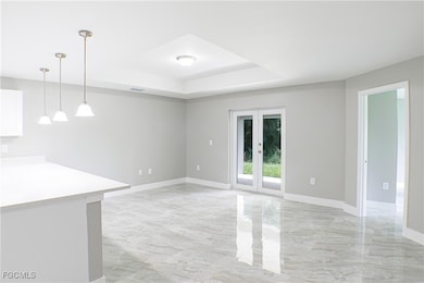 Unfurnished living room featuring a tray ceiling, french doors, and light marble finish flooring