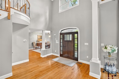 Entryway featuring light wood-style flooring, a chandelier, a high ceiling, and ornate columns