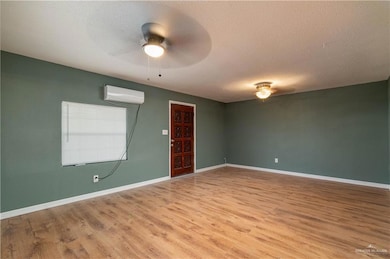 Empty room with baseboards, a ceiling fan, a textured ceiling, wood finished floors, and a wall unit AC