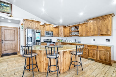 Kitchen with appliances with stainless steel finishes, vaulted ceiling, open shelves, wood tiled floors, and brown cabinets