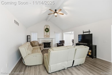 Living area featuring beamed ceiling, a premium fireplace, light wood-style floors, ceiling fan, and high vaulted ceiling