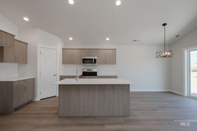 Kitchen featuring stainless steel appliances, recessed lighting, decorative light fixtures, light wood finished floors, and an island with sink