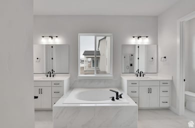 Bathroom featuring a shower stall, a garden tub, two vanities, and light marble finish flooring