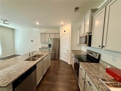 Kitchen with stainless steel appliances, dark wood-style flooring, a center island with sink, light stone counters, and recessed lighting