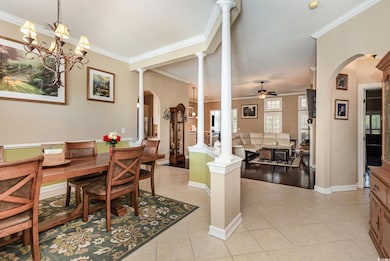 Dining space with arched walkways, crown molding, ceiling fan, light tile patterned floors, and decorative columns