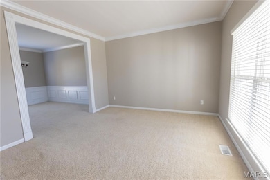 Empty room with crown molding, carpet floors, and a wainscoted wall