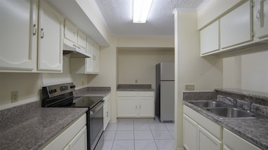 A spacious kitchen with ample cabinet storage and counter space. It features modern appliances, including a stainless steel refrigerator and a stove, complemented by a neutral palette and tiled flooring.