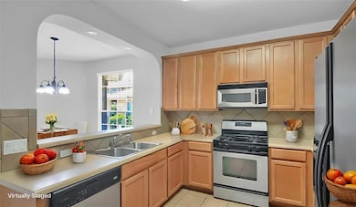 Kitchen featuring appliances with stainless steel finishes, decorative backsplash, light countertops, a peninsula, and hanging light fixtures