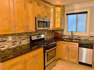 Kitchen featuring appliances with stainless steel finishes, a sink, dark stone counters, tasteful backsplash, and light tile patterned flooring