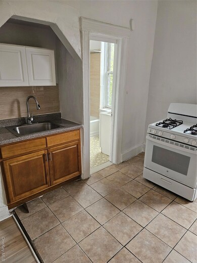 Kitchen featuring stove, dark countertops, light tile patterned floors, backsplash, and brown cabinetry