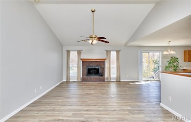 Unfurnished living room with healthy amount of natural light, vaulted ceiling, light wood-style flooring, a brick fireplace, and a ceiling fan