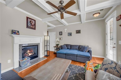 Living area featuring coffered ceiling, ceiling fan, wood finished floors, beam ceiling, and a premium fireplace