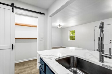 Kitchen featuring baseboards, a barn door, a sink, light wood finished floors, and light stone counters