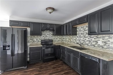 Kitchen with black appliances, dark cabinets, tasteful backsplash, dark wood-style flooring, and under cabinet range hood
