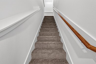 This image shows a carpeted staircase with a wooden handrail on the right side, leading to an upper floor with white walls.
