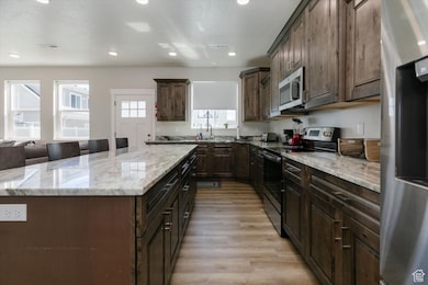 Kitchen with stainless steel appliances, dark brown cabinets, recessed lighting, a kitchen island, and light stone countertops