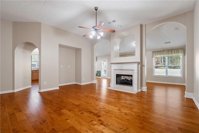 Unfurnished living room with arched walkways, plenty of natural light, wood finished floors, a ceiling fan, and a textured ceiling
