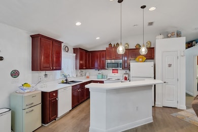 Kitchen featuring reddish brown cabinets, light countertops, lofted ceiling, light wood-style floors, and recessed lighting