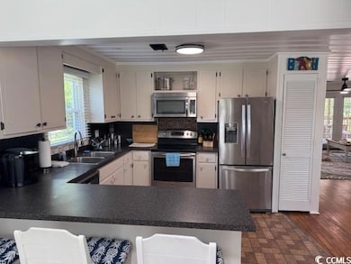 Kitchen featuring stainless steel appliances, dark countertops, a peninsula, and tasteful backsplash
