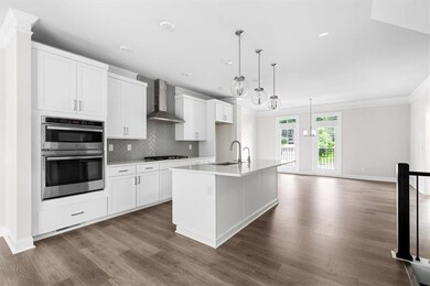 Kitchen featuring wall chimney range hood, double oven, a sink, black gas stovetop, and white cabinets