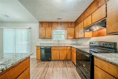 Kitchen featuring black appliances, under cabinet range hood, a sink, light wood-type flooring, and brown cabinets