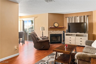 Living area featuring wood finished floors, a brick fireplace, baseboards, and a textured ceiling