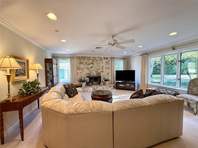 Living area with ornamental molding, a stone fireplace, light colored carpet, a ceiling fan, and recessed lighting