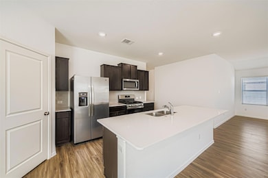 Kitchen with stainless steel appliances, tasteful backsplash, light wood-style flooring, a kitchen island with sink, and dark brown cabinetry