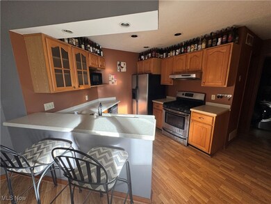 Kitchen featuring a kitchen bar, appliances with stainless steel finishes, light countertops, glass insert cabinets, and light wood finished floors