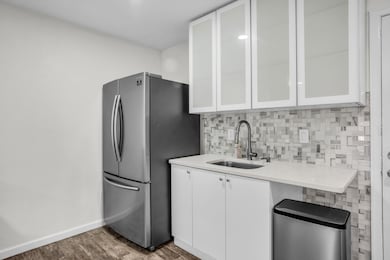 Kitchen featuring white cabinetry, freestanding refrigerator, decorative backsplash, glass insert cabinets, and dark wood-type flooring