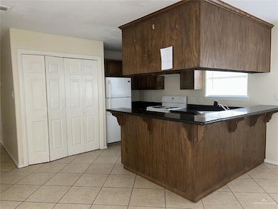 Kitchen with electric range oven, freestanding refrigerator, a breakfast bar area, light tile patterned floors, and a peninsula