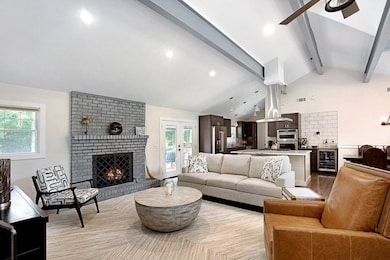 Living room with vaulted ceiling with beams, wine cooler, light hardwood / wood-style floors, brick wall, and a fireplace