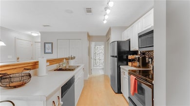 Kitchen with stainless steel appliances, white cabinets, light countertops, crown molding, and light wood-style floors