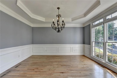 Empty room featuring a raised ceiling, plenty of natural light, a chandelier, ornamental molding, and light wood finished floors