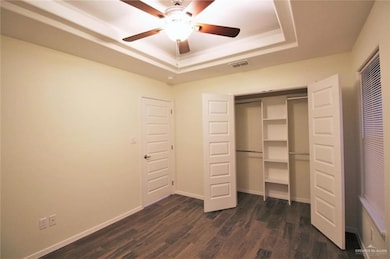 Unfurnished bedroom featuring a tray ceiling, dark wood finished floors, a closet, and ceiling fan