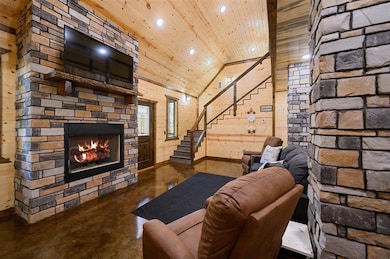 Unfurnished living room featuring a stone fireplace, high vaulted ceiling, concrete floors, wooden walls, and wood ceiling