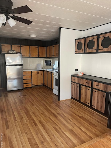 Kitchen with light wood-type flooring, fridge, light countertops, stainless steel gas stove, and brown cabinets