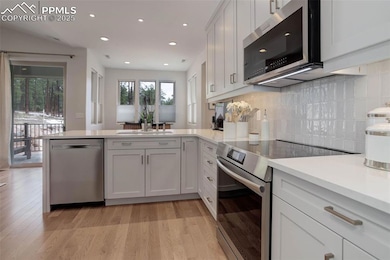 Kitchen featuring stainless steel appliances, a peninsula, light countertops, light wood finished floors, and backsplash
