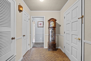 Corridor featuring ornamental molding, a textured ceiling, and brick floors