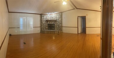 Unfurnished living room with wood finished floors, a stone fireplace, ceiling fan, ornamental molding, and wainscoting