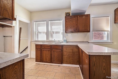 Kitchen with light countertops, a peninsula, light tile patterned flooring, and brown cabinets