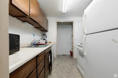 Kitchen with white appliances, light countertops, a textured ceiling, and dark brown cabinets