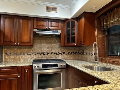 Kitchen with gas range, granite counters, glass insert cabinets, under cabinet range hood, and ornamental molding