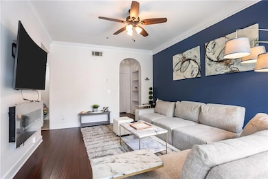 Living area featuring arched walkways, ceiling fan, crown molding, and hardwood / wood-style flooring