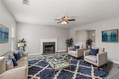 Living area featuring wood finished floors, baseboards, ceiling fan, and a fireplace with raised hearth