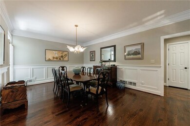 Dining space featuring a chandelier, ornamental molding, dark wood-type flooring, wainscoting, and a decorative wall